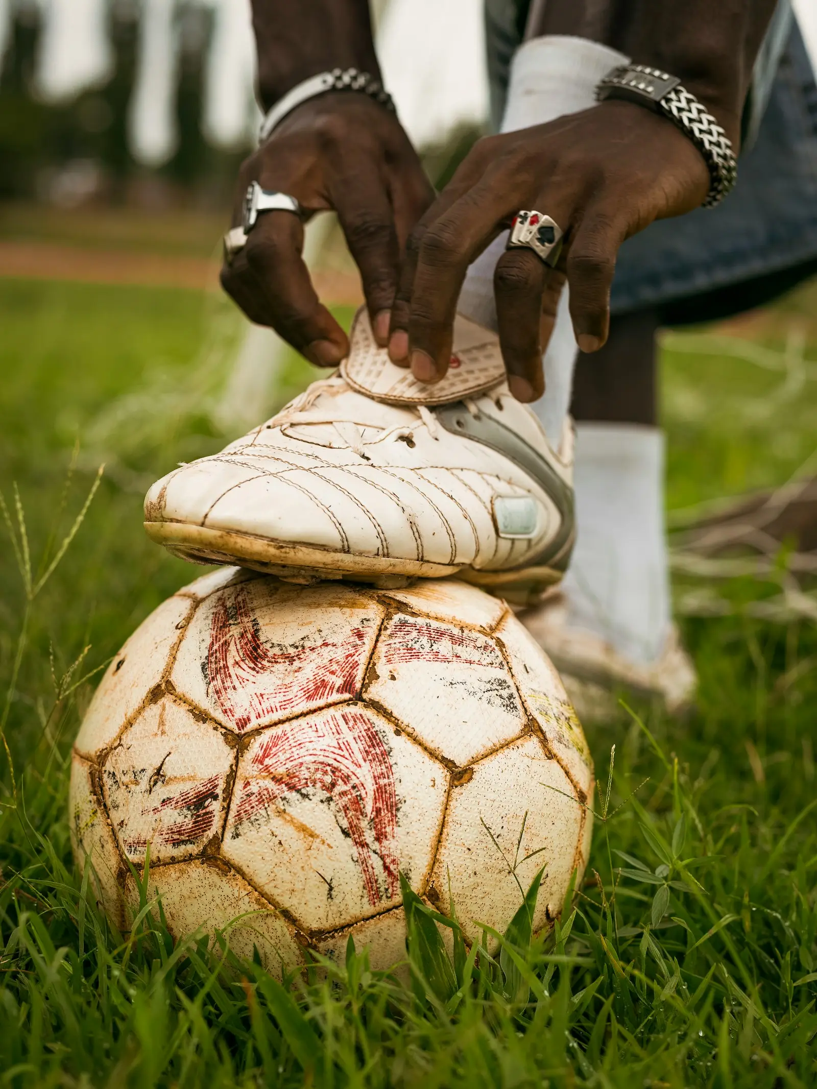Hands tying the laces of a worn white football boot resting on an old ball