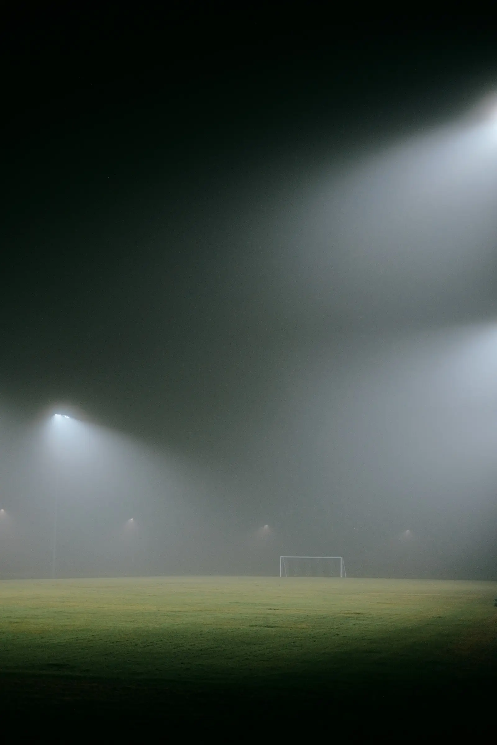Fog hanging under the floodlights over an empty pitch at night