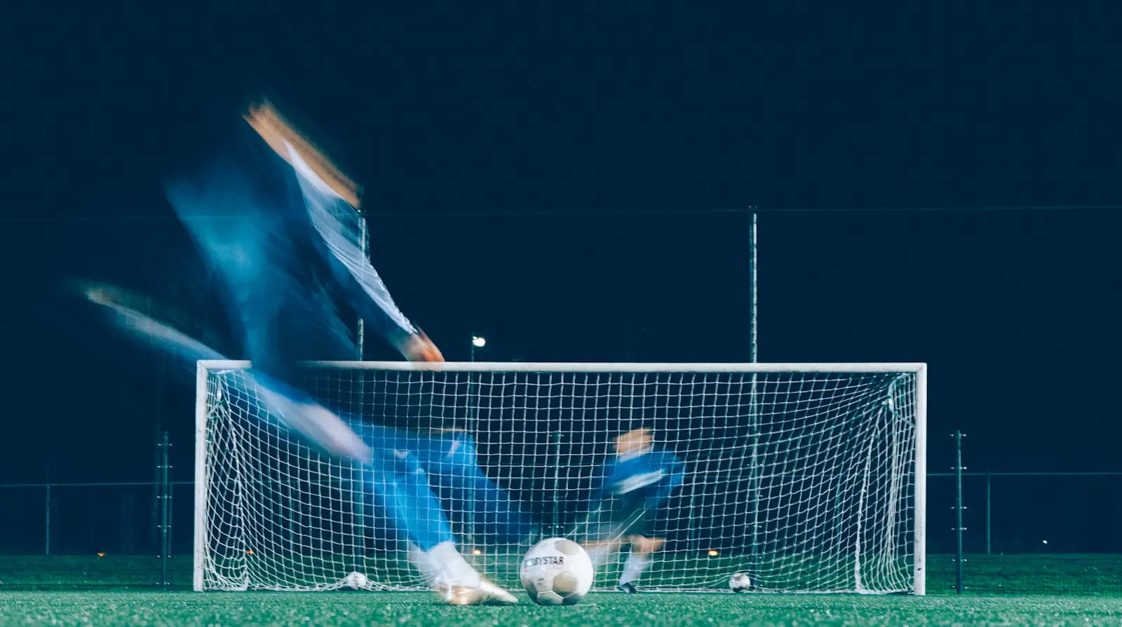 A volley struck under floodlights, the player a blur of motion in front of the goal