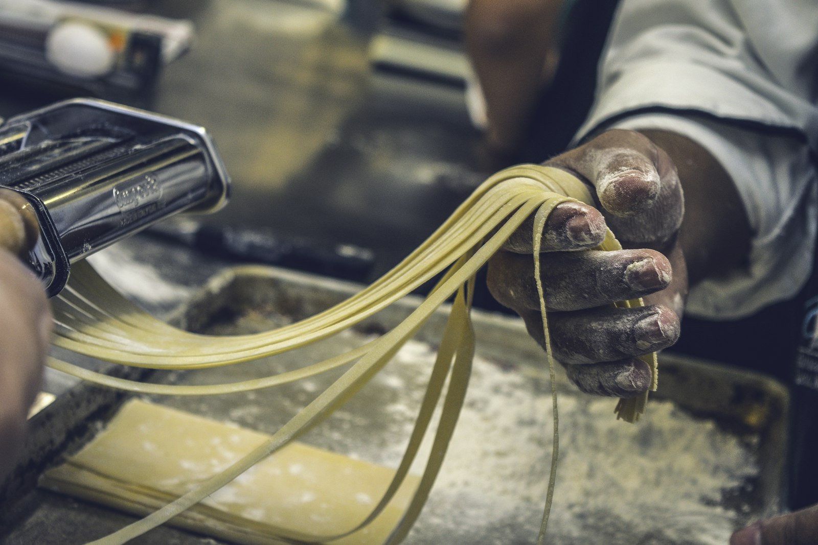 Hands feeding fresh pasta sheets through a machine