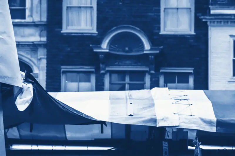 The striped awning of a market stall in front of a brick shopfront, printed in Prussian blue.