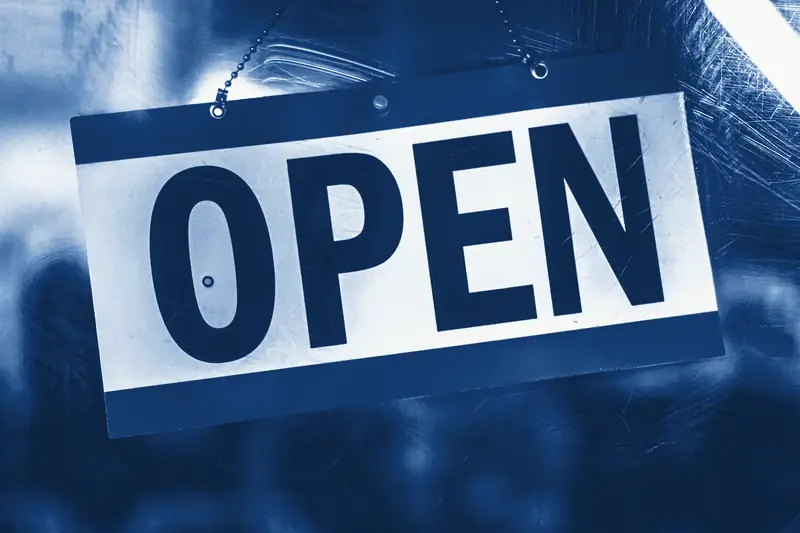An OPEN sign hanging on a chain behind a scratched glass shop door, printed in Prussian blue.