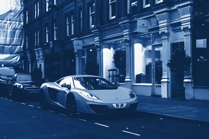A row of shops on a town street, with a sports car parked outside, printed in Prussian blue.